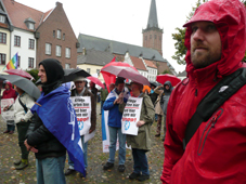 Demonstranten mit Plakaten und aufgespannten Regenschirmen auf dem Marktplatz vor dem Rathaus in Kalkar.