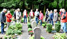 Friedhof: Menschen im Halbkreis um Grabstätten.