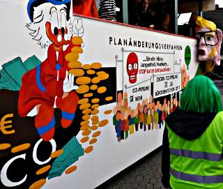 Bemalter Karnevalswagen: Donald Duck-Dekkers mit Goldstücken und Geldscheinen auf CO-Röhre. »Planänderungsverfahren. … Erkarth, Hilden, Langenfeld, Monheim… STOP Bayer Giftgasröhre! CO-Pipeline NEIN. Gegen CO-Pipeline JA. Bürgerentscheid 2011«.