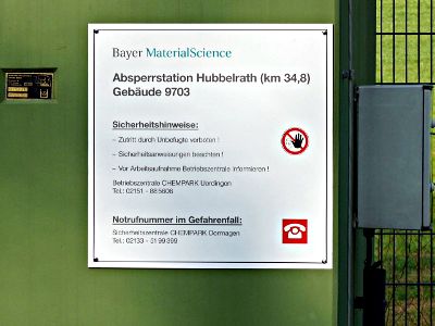 Schieberstation mit Eisengittertür und Warnschild: »Bayer MaterialScience. Absperrstation Hubbelrath (km 34,8) Gebäude 9703. Sicherheitshinweise: Zutritt durch Unbefugte verboten! Sicherheitsanweisungen beachten! Vor Arbeitsaufnahme Betriebszentrale informieren! Betriebszentrale CHEMPARK Uerdingen Tel.: 02151 885606. Notrufnummer im Gefahrenfall: Sicherheitszentrale CHEMPARK Dormagen Tel.: 02133 5199399«.